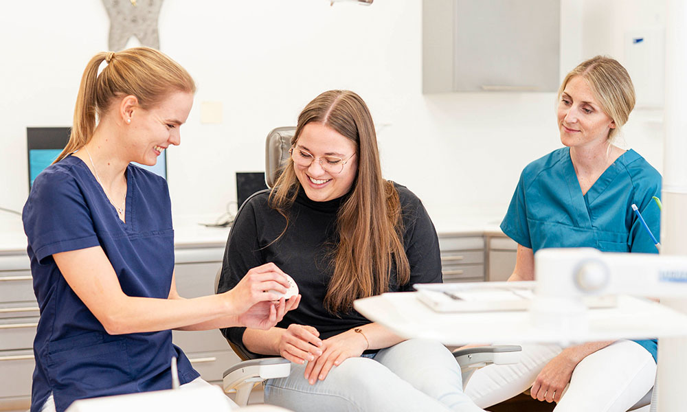 Zahnarztteam in der Zahnarztpraxis betreut eine Patientin beim Zahnarztstuhl bei der Behandlung