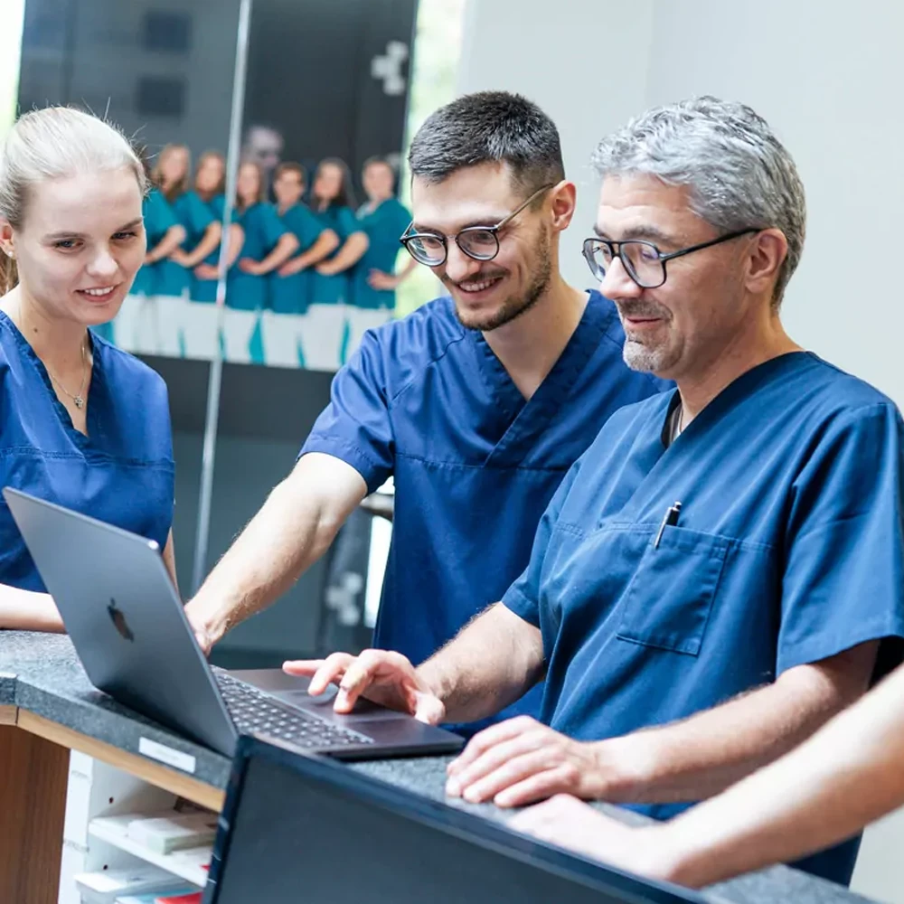 Zahnarztteam in der Praxis berät am Laptop – Hightech im Arbeitsalltag der Zahnarztfamilie Scherg.